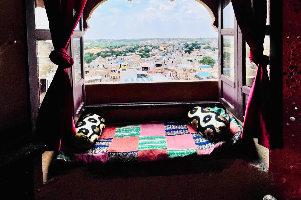 Une fenêtre donnant sur un paysage urbain, un coussin à motifs et un rideau rouge.