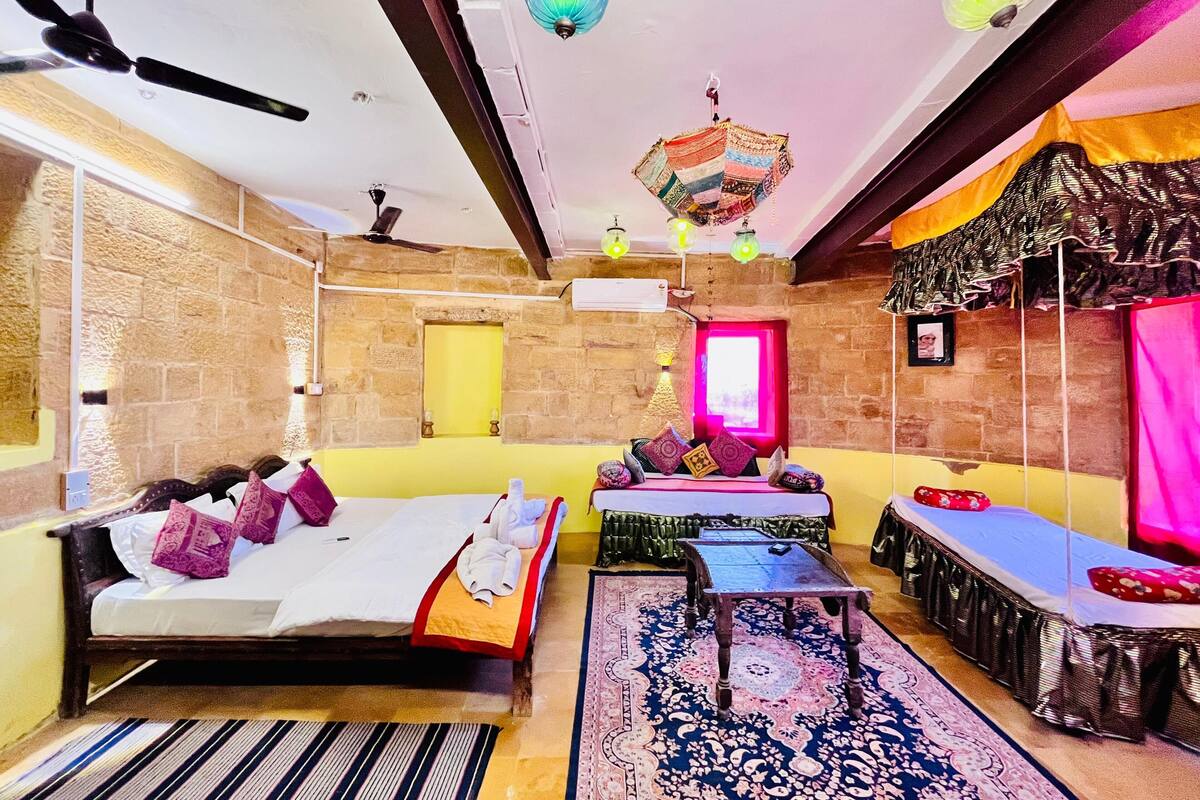 Une chambre d’hôtel avec un lit, une petite table, un canapé, un tapis à motifs et une lampe décorative suspendue au plafond.