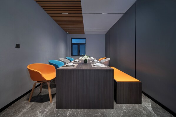 Une salle de conférence moderne, dotée d’une longue table, de chaises orange et bleues, et d’une grande fenêtre.