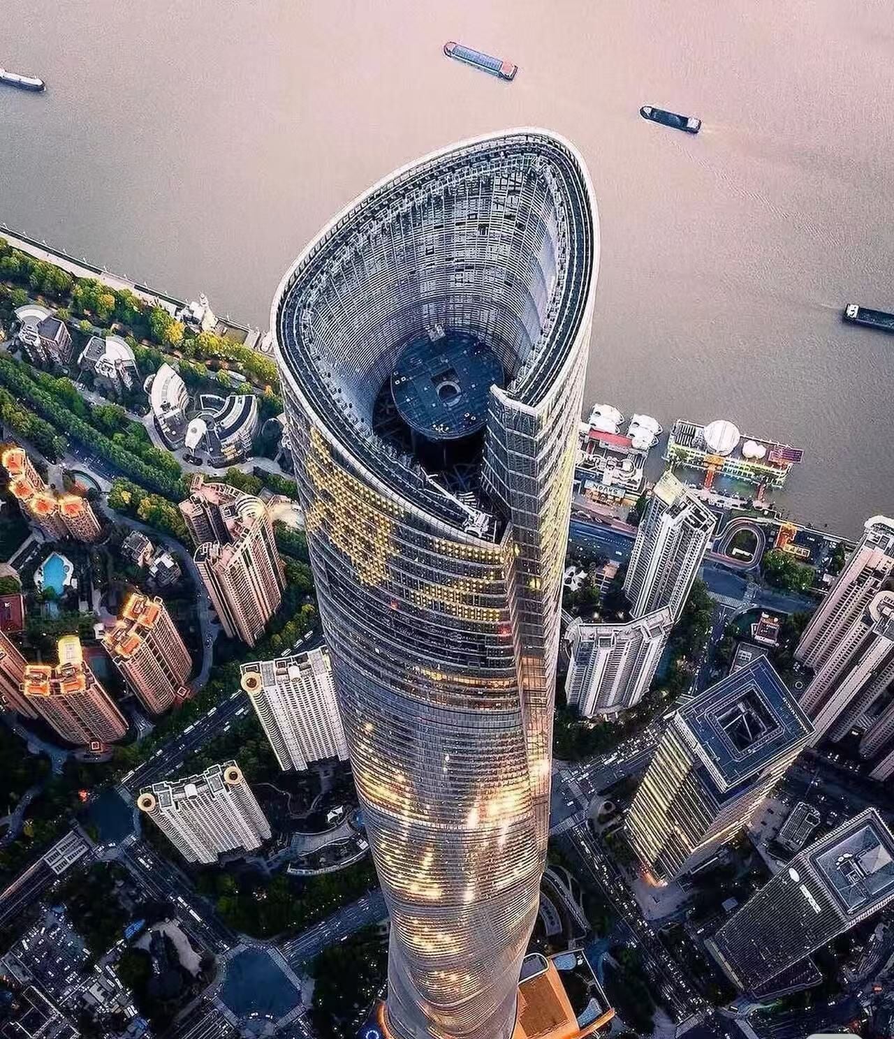 Um edifício alto com um design curvo singular, rodeado por outros edifícios modernos e por uma massa de água.