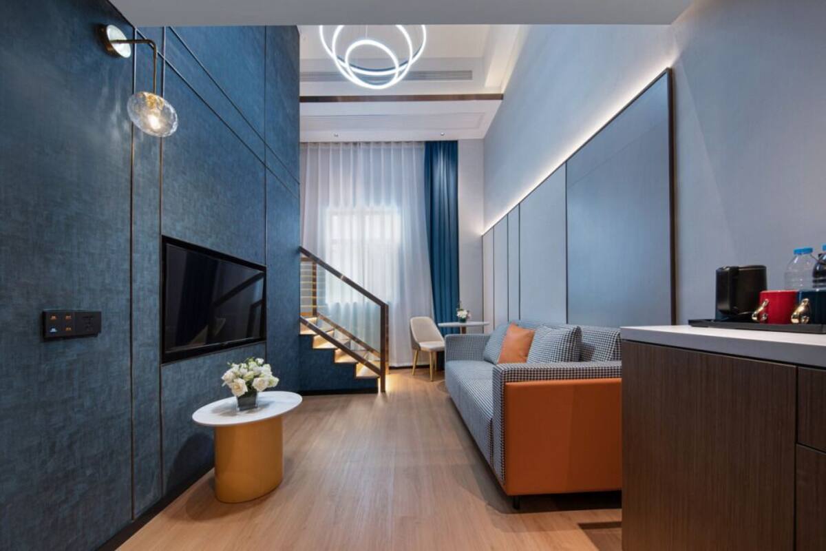 Una sala de estar moderna con un televisor de pantalla plana, una mesa de centro redonda con flores, un sofá y una escalera que lleva a otro nivel.