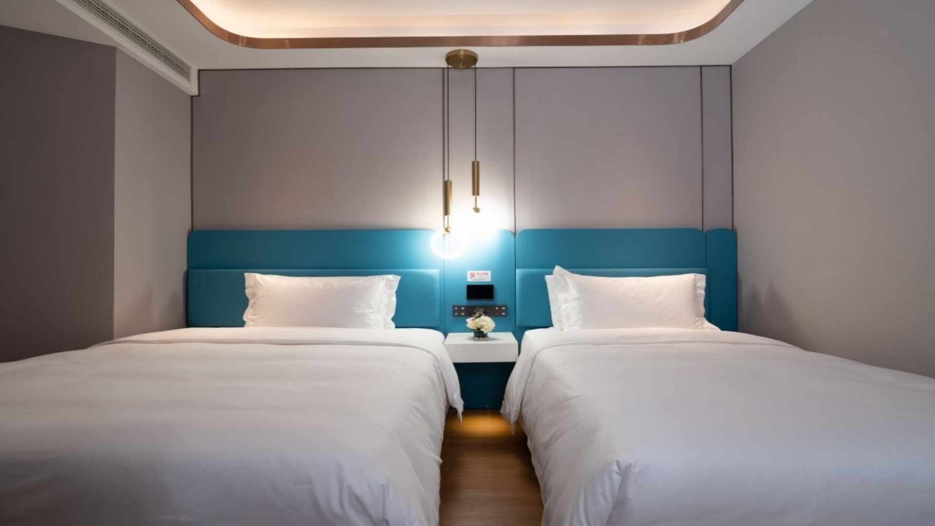 A hotel room with two beds, a nightstand with a lamp, and a wall-mounted light fixture.