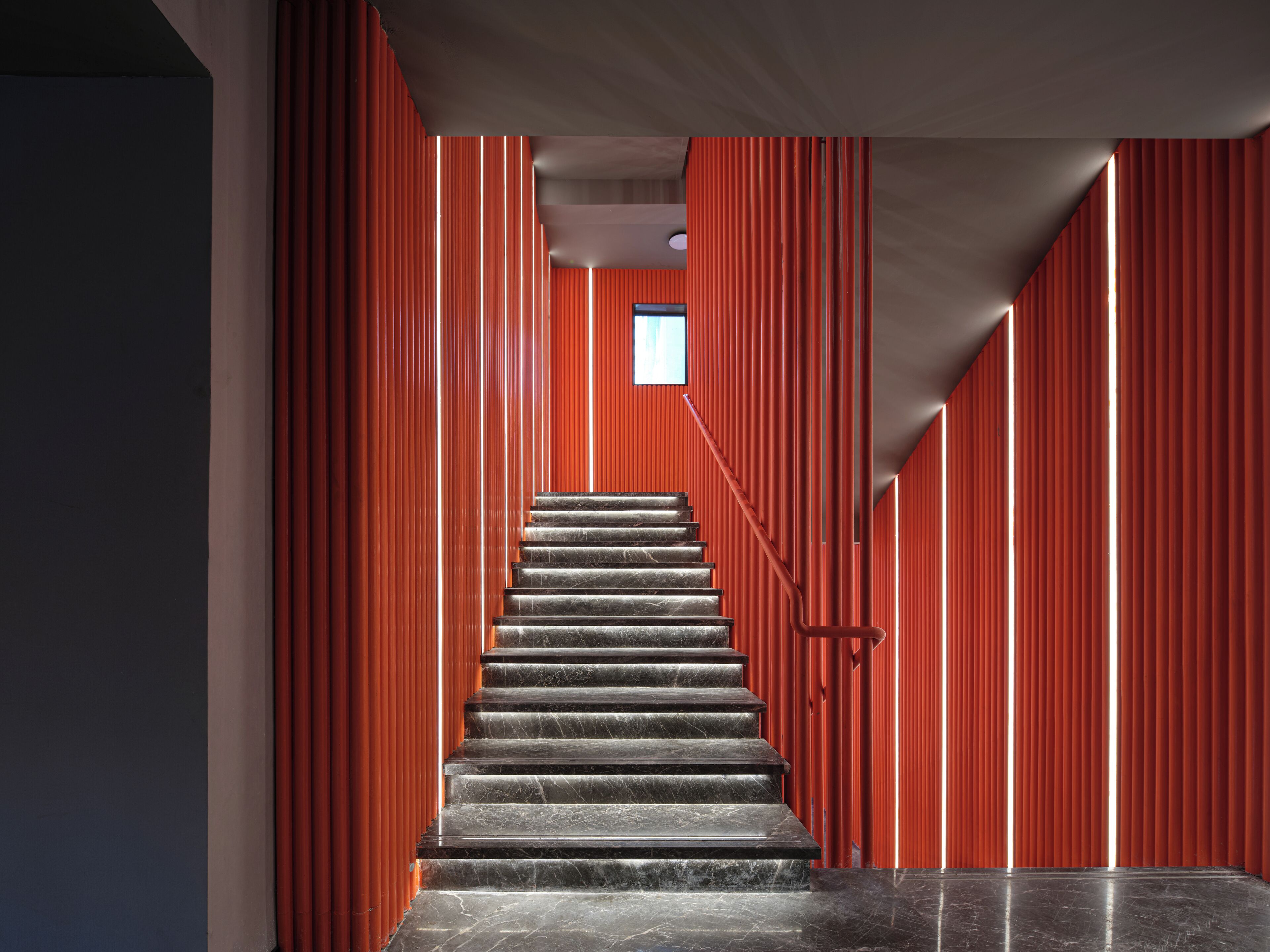 Una escalera con una pared roja a un lado y un piso oscuro.