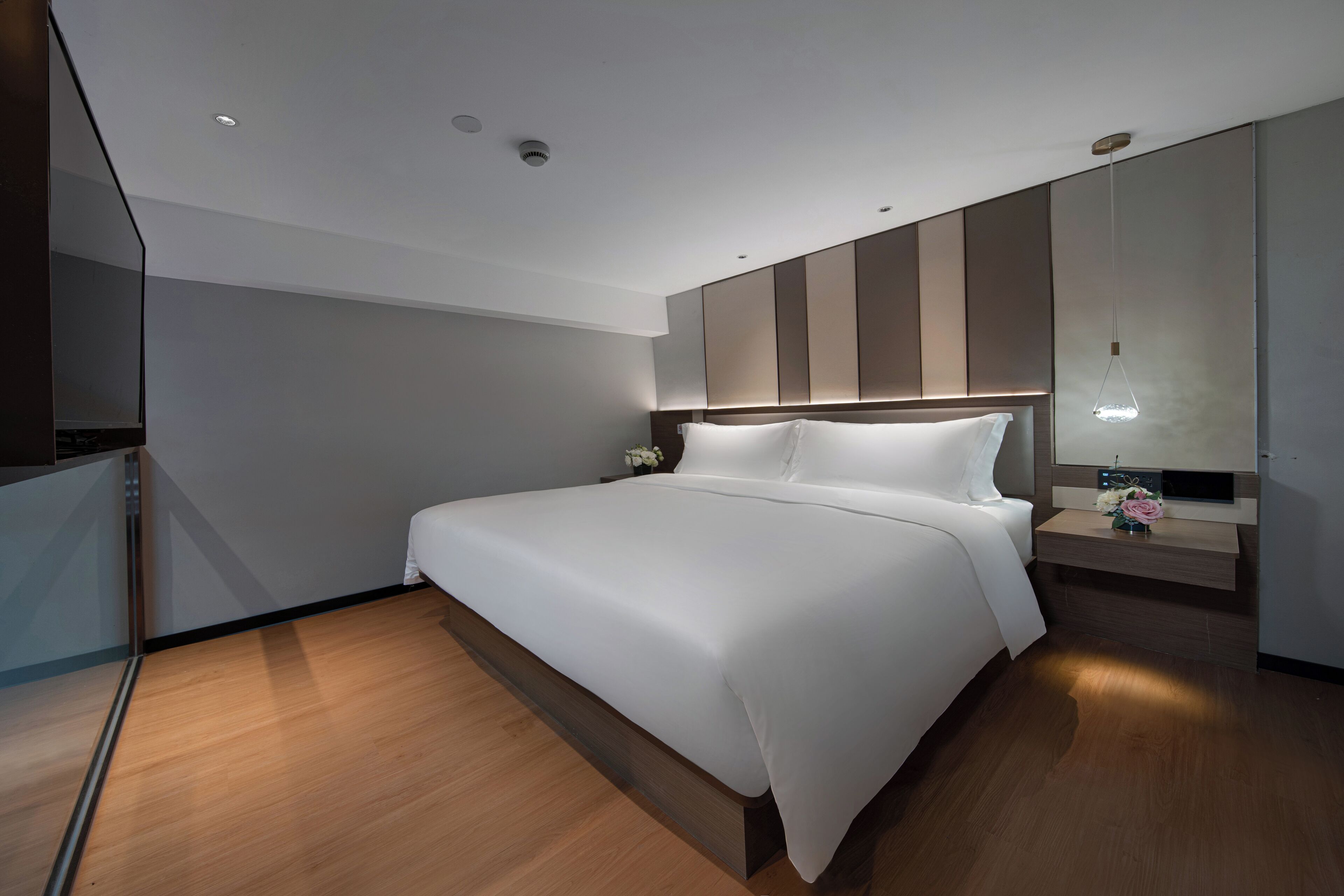 A modern hotel room with a large bed, a bedside table with a lamp, and a large mirror above the bed.