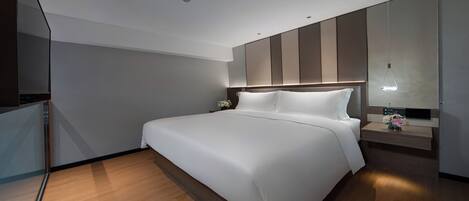 A modern hotel room with a large bed, a bedside table with a lamp, and a large mirror above the bed.