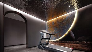 Una habitación moderna con una caminadora, un gran mural de una escena espacial y un piso de piedra pulida.