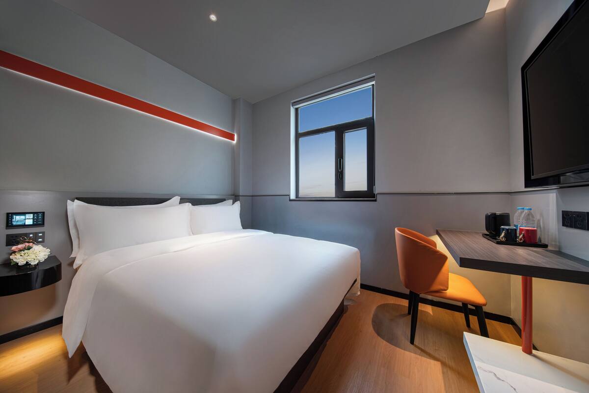 Habitación de hotel con una cama grande, un escritorio con silla, un televisor y una ventana.