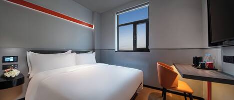 A hotel room with a large bed, a desk with a chair, a TV, and a window.