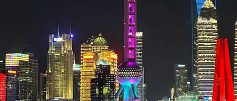 Een stadsgezicht bij nacht met verlichte gebouwen, waaronder een toren met een bolvormig uitkijkplatform en een brug met blauwe verlichting.