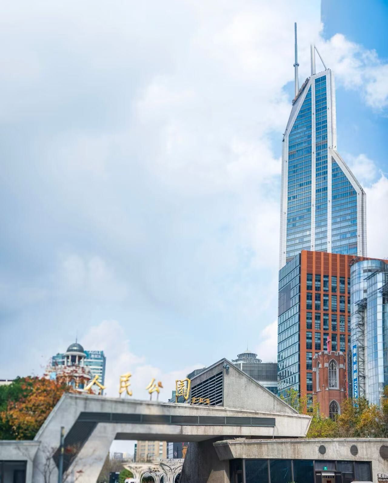 Un paisaje urbano moderno con un rascacielos destacado, un puente y un edificio con caracteres chinos.