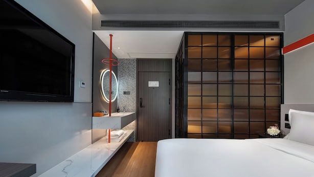 Habitación de hotel moderna con una cama grande, un televisor montado en la pared, un baño con tocador y una puerta corrediza estilo shoji.