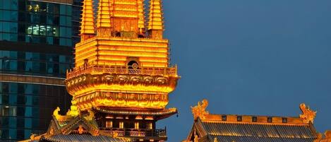 A traditional multi-tiered temple with ornate golden roofs and intricate architectural details, set against a modern city skyline.