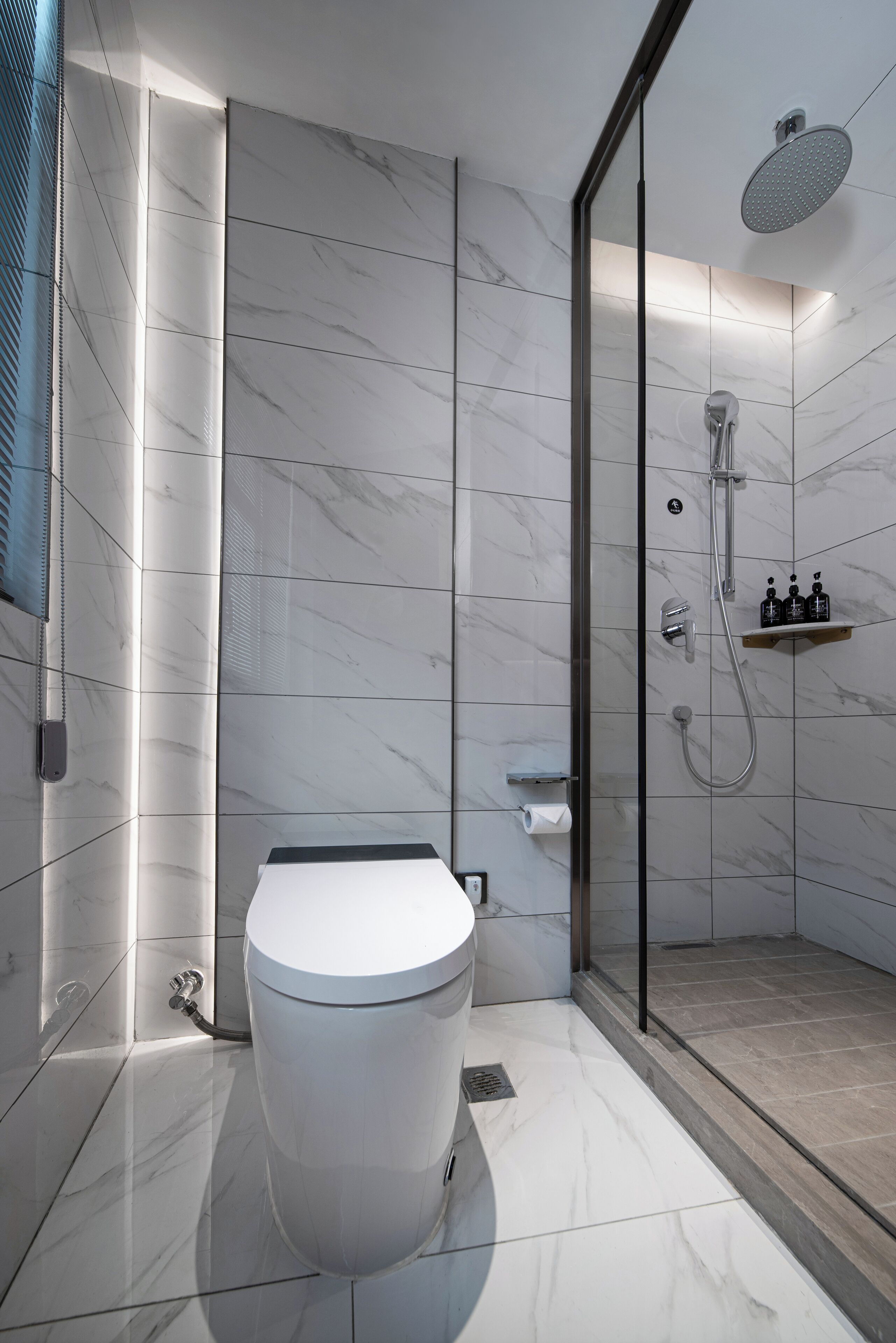 Un baño moderno con inodoro independiente, zona de ducha con mampara de vidrio y suelo de mármol.