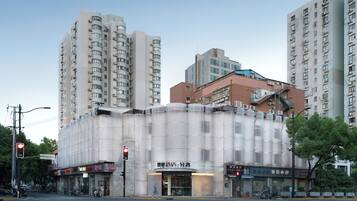 A modern building with a unique cylindrical facade, located at a city intersection with traffic lights and surrounding high-rise buildings.