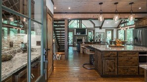 A spacious kitchen with a large island, wooden flooring, and a stone fireplace. - Harmony River Retreat ~ Hot Tub ~ Fire Pit ~ Fish/Tube from the Backyard! (Ellijay)