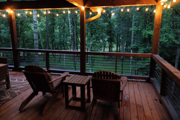 A wooden deck with chairs and a table, overlooking a forested area.