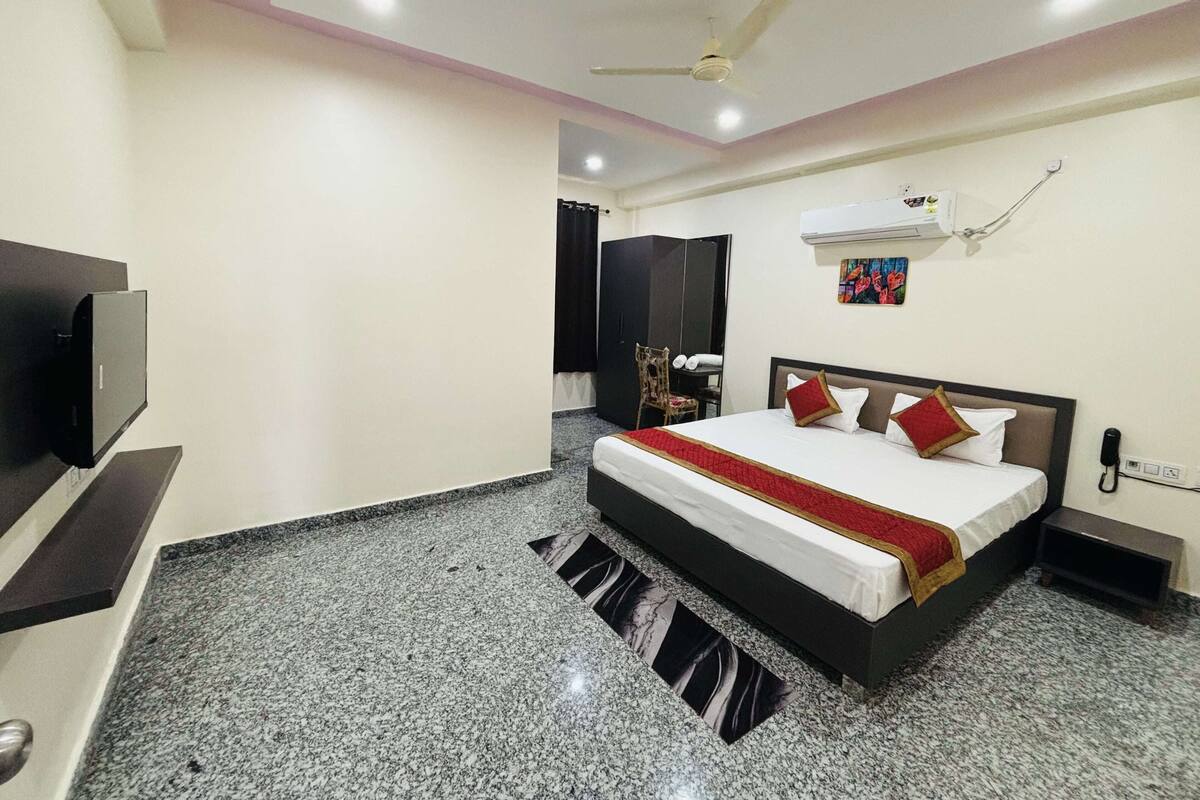 A hotel room with a bed, a TV, a ceiling fan, and a wall-mounted air conditioner.
