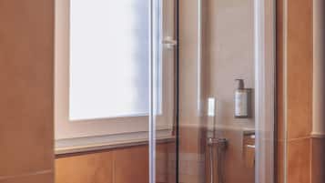A glass-enclosed shower with a handheld showerhead, a bottle of shampoo, and a towel rack.