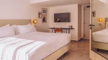 A hotel room with a large bed, a desk with a chair, a television, and framed artwork on the walls.