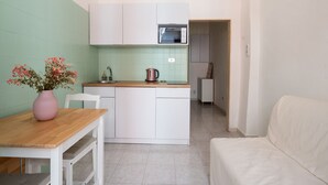 A compact kitchen with white cabinets, a wooden countertop, and a pink vase with flowers. - Rifugio Pugliese by Wonderful Italy (Bari)
