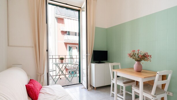 A bedroom with a bed, a desk with a TV, a small table with chairs, and a balcony with a view of buildings. - Rifugio Pugliese by Wonderful Italy (Bari)