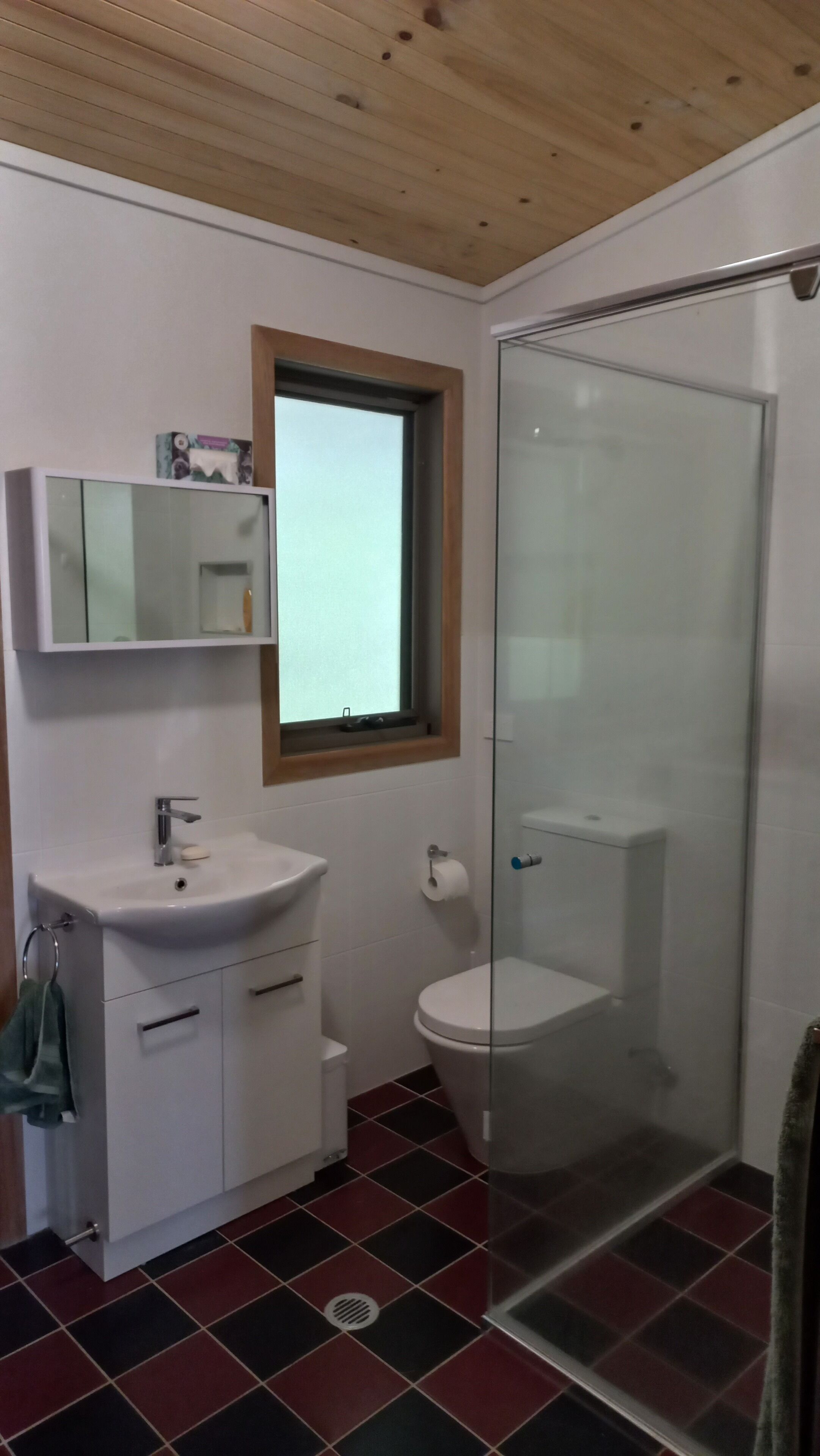 A bathroom with a white sink, mirror, and toilet. There is a window above the sink and a glass shower enclosure.
