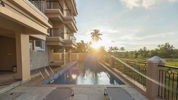 A swimming pool with lounge chairs, a view of palm trees, and a building with balconies. - Palm Retreat 1BHK Pool & Field Views (Calangute)