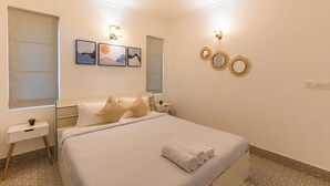 A neatly arranged bedroom with a bed, bedside tables, and wall-mounted decor. - Palm Retreat 1BHK Pool & Field Views (Calangute)