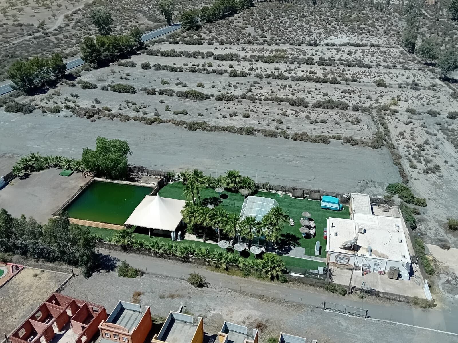 Vista aérea de un complejo turístico con piscina, cancha de tenis y zona de estacionamiento.