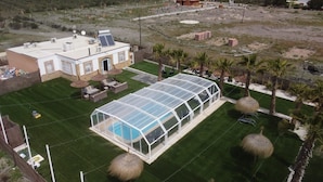 A large greenhouse structure with a pool, surrounded by a well-maintained lawn and palm trees. - Villa 'Dehesa' with Mountain Views, Wi-Fi, and Air Conditioning (Tabernas)