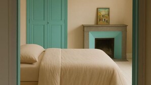 Un dormitorio con cama, un armario color turquesa y una chimenea con un cuadro encima.