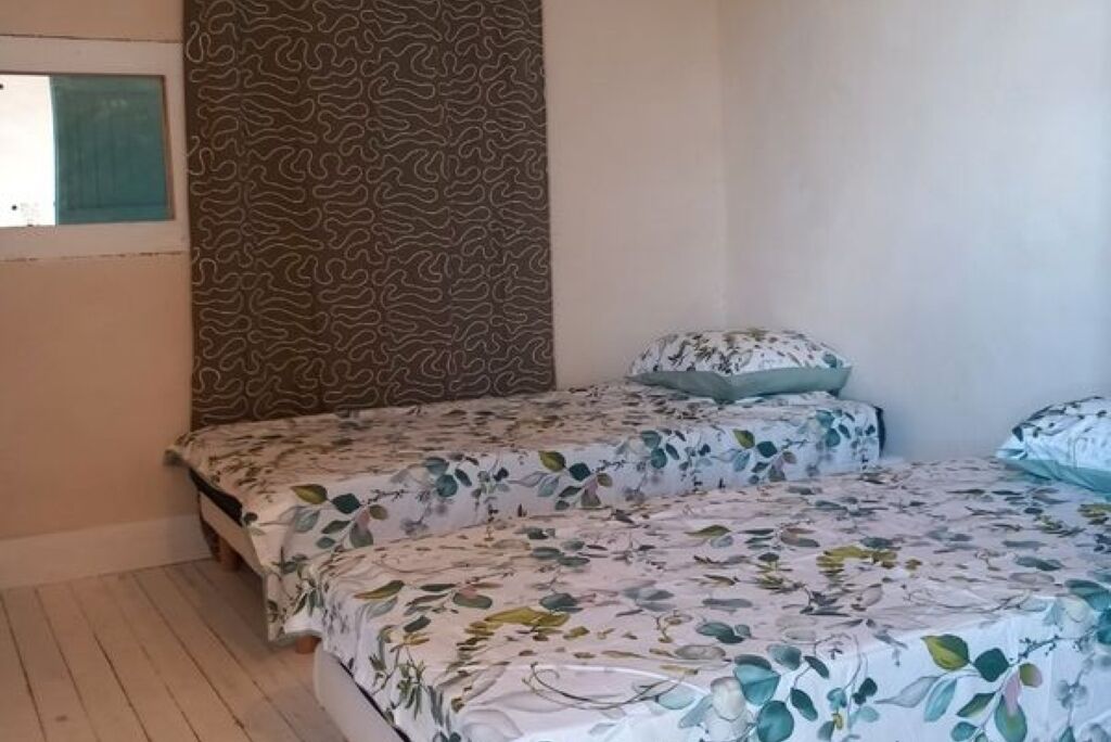 Une chambre avec deux lits, chacun agrémenté de draps à motifs floraux, d’une tête de lit décorée et d’une fenêtre offrant une vue agréable.