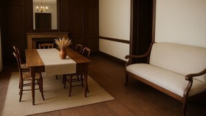 Un comedor con una mesa de madera, sillas, un florero con plantas secas y un sofá.