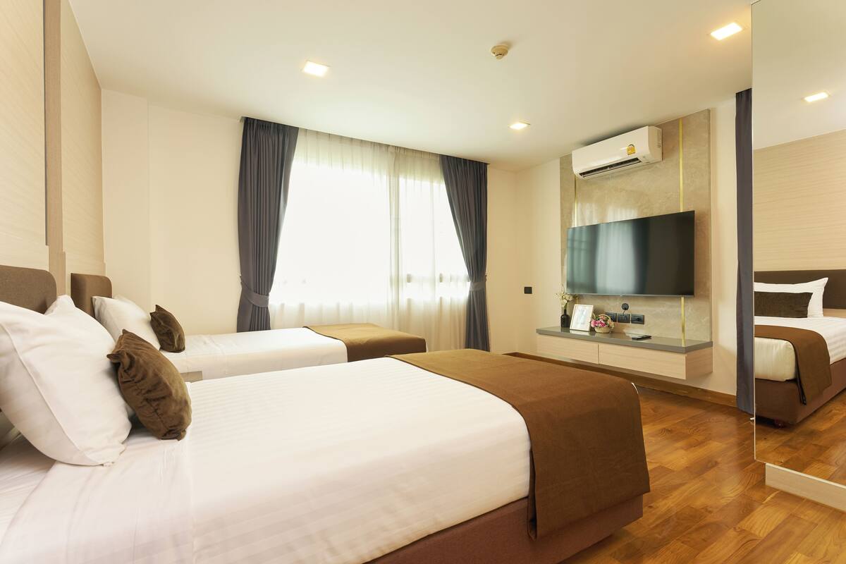 A hotel room with two beds, a flat-screen TV, a mirror, and a window with curtains.