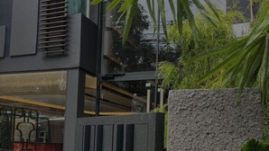 A modern building with a glass facade, a concrete planter with a palm plant, and a metal gate. - Shine Thonglor (Bangkok)