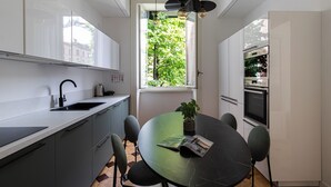 A modern kitchen with a dining area, featuring a large window, built-in appliances, and a green table.