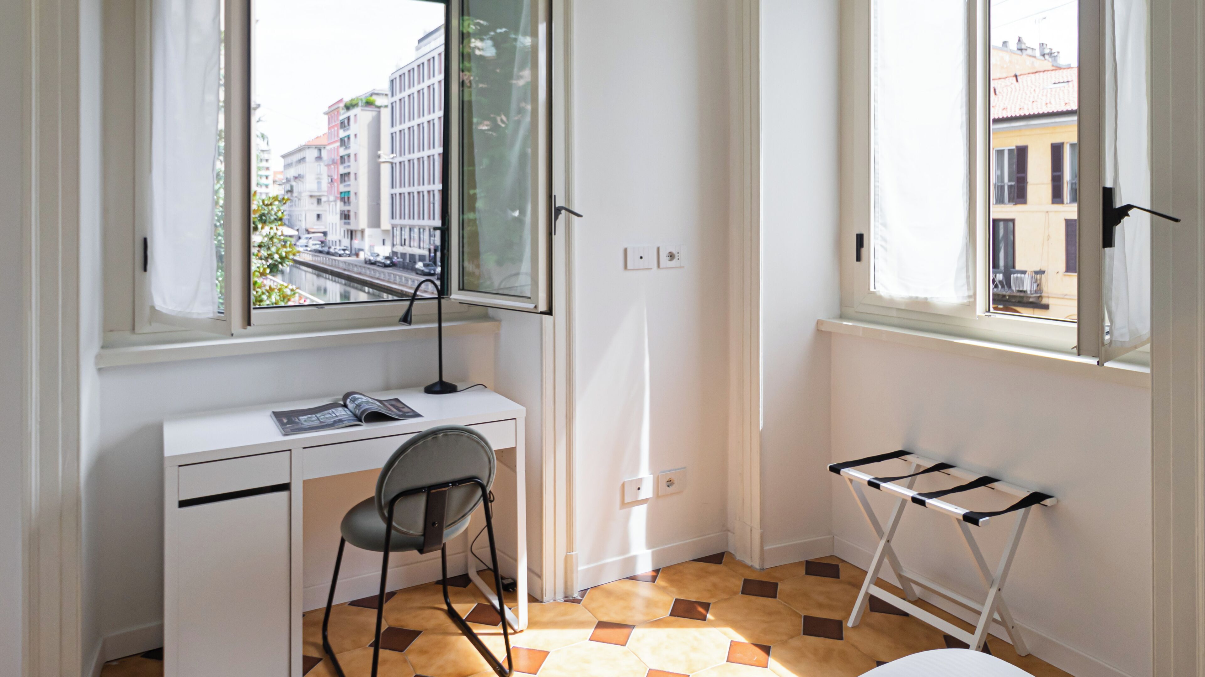 A small, bright room with a desk, chair, and a window overlooking a city street.