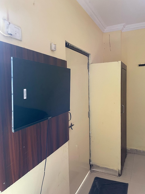 Quarto com televisão de tela plana presa a um painel de madeira, armário bege e porta com puxador de metal.