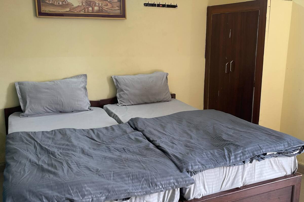 Een slaapkamer met een bed, twee kussens, een houten garderobe, een kapstok aan de muur en een lijst met een foto.