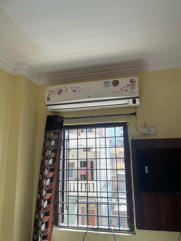 A room with a window, a curtain, and an air conditioning unit mounted on the wall. - Nandini Guest House  (Hyderabad)