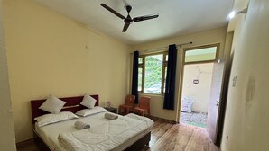A bedroom with a bed, a ceiling fan, a window with curtains, and a view of the outside. - AP Residency Yamunotri (Rajgarhi)