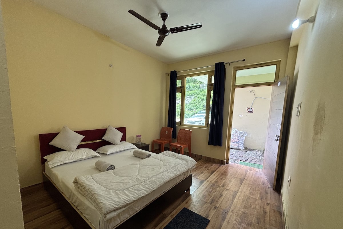 Un dormitorio con cama, ventilador de techo, ventana con cortinas y vista al exterior.