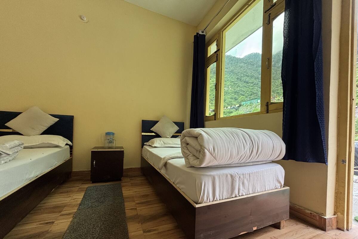Un dormitorio con dos camas, una mesita de noche, un dispensador de agua y vistas a un bosque por la ventana.