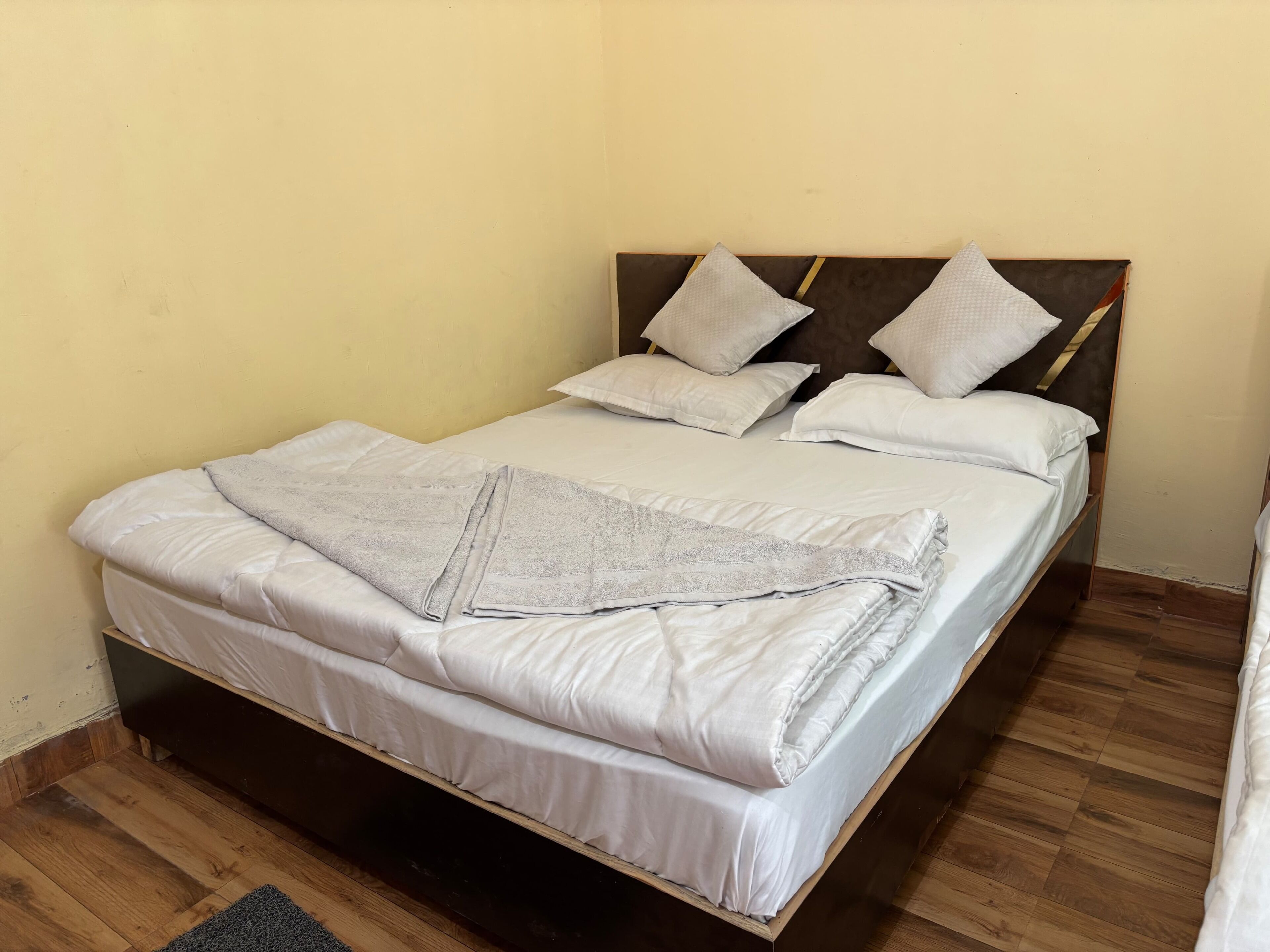 A single bed with a wooden headboard, white bedding, and a grey blanket.