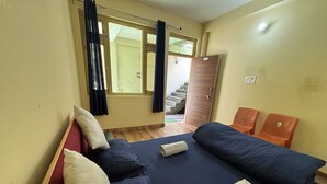 A room with a bed, two chairs, a window with curtains, and a door leading outside. - AP Residency Yamunotri (Rajgarhi)