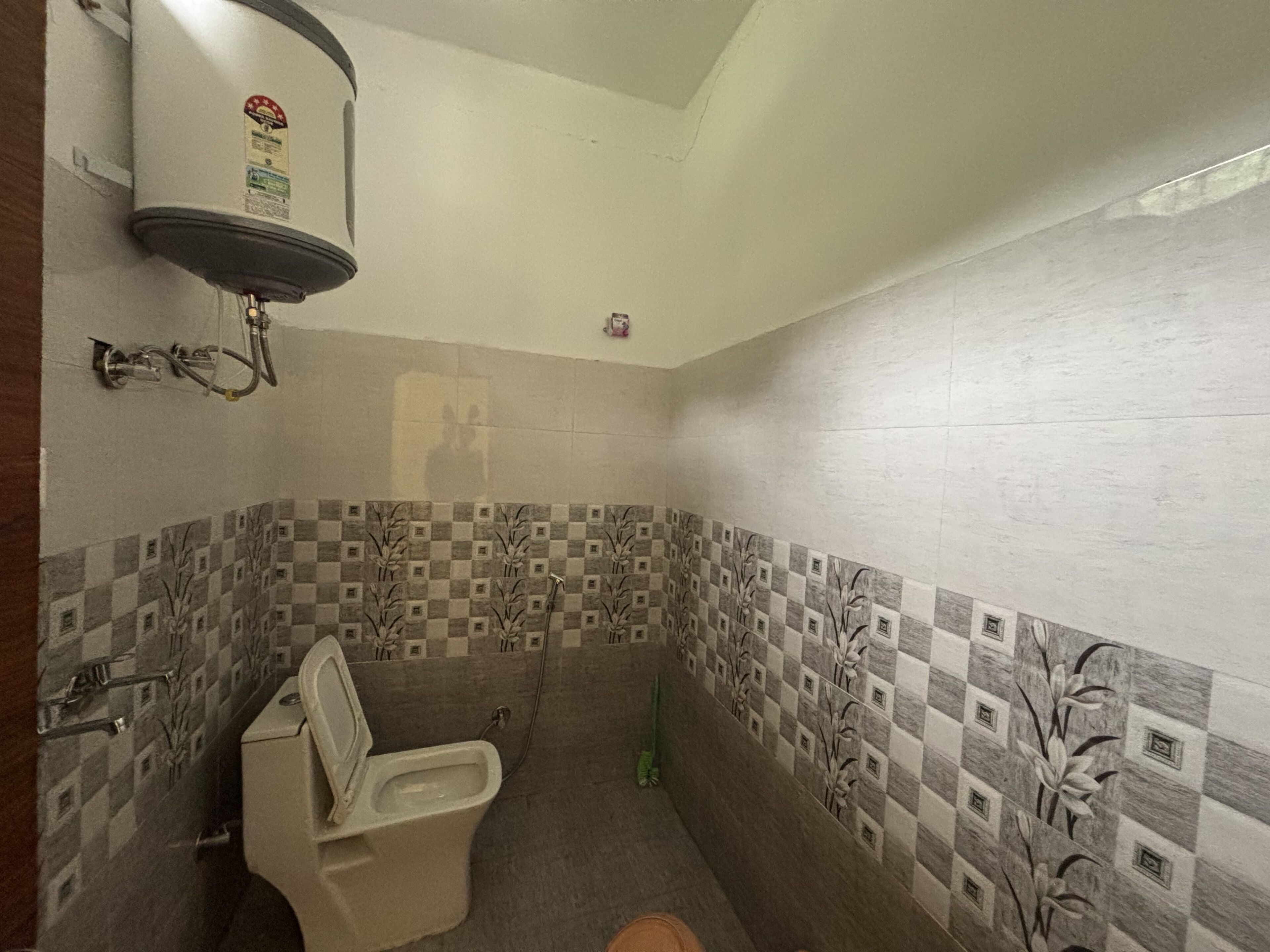 Un baño con inodoro, calentador de agua y azulejos de pared a cuadros.