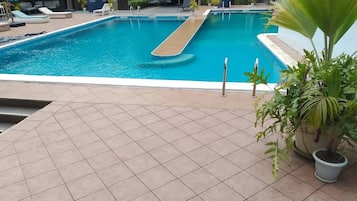Uma piscina com espreguiçadeiras e guarda-sóis, rodeada por plantas em vasos.