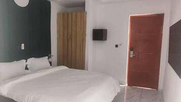 Un dormitorio con una cama, un televisor en la pared, una puerta y una cortina.