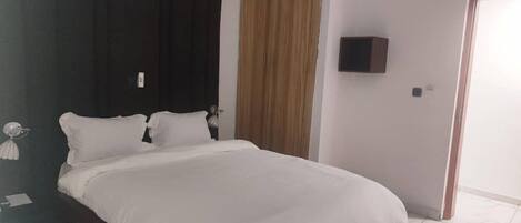 Een moderne slaapkamer met een groot bed, donker paneelwerk aan de wand, een houten garderobe en een aan de muur bevestigde televisie.