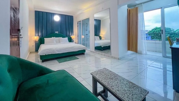Habitación de hotel con dos camas, un sofá verde, una mesita pequeña y un balcón con vistas.